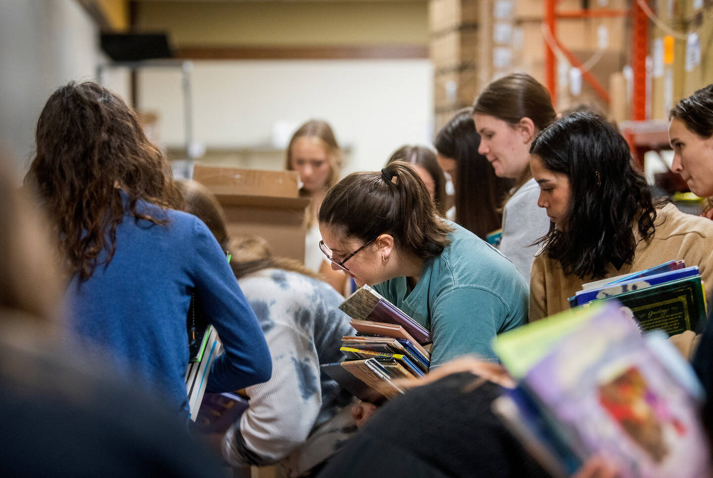 A group of people are gathered in a warehouse, sorting through stacks of books and magazines.